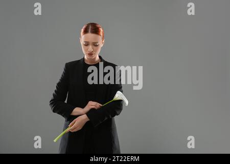 Traurige Frau mit Calla-Lilienblume auf grauem Hintergrund, Platz für Text. Beerdigungszeremonie Stockfoto