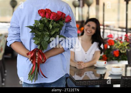 Internationale Dating. Mann, der einen Rosenstrauß für seine geliebte Frau im Restaurant versteckt, selektiver Fokus Stockfoto