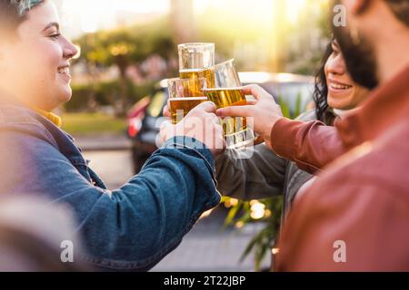 Eine vielfältige Gruppe von Freunden, darunter eine Frau mit leuchtenden kurzen Haaren, hebt ihre Biergläser in einem Toast auf einem Bürgersteig Stockfoto