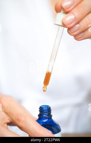 Eine kurze Seitenaufnahme einer blauen Flasche mit Serum, Tropfen, die von einer Pipette fallen. Nahaufnahme von Tropfen feuchtigkeitsspendendes Serum für die Haut. Ein Produkt für MID Stockfoto
