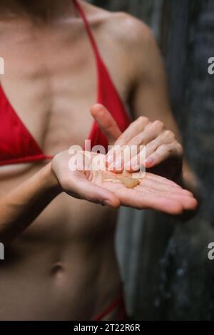 Vertikales Foto einer Frau in der Dusche, die Duschgel aus einem Glas drückt und ihre Hände seift. Schaum aus Duschgel und Seifenstruktur in der Frauenhand Stockfoto