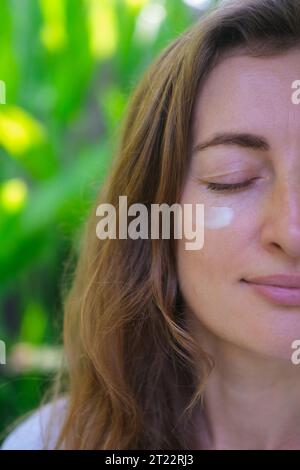 Nahaufnahme des Gesichts einer Frau, die ihr feuchtigkeitsspendende und pflegende Creme auf das Gesicht aufträgt. Eine Frau trägt Creme auf ihr Gesicht mit leichten Massagebewegungen auf Stockfoto