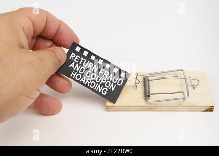 Ein Mann zieht den Köder aus einer Mausefalle. Köder, ein Blatt schwarzes Papier mit der Aufschrift - Return-Betrug und Gutscheinhorten. Finanz- und Rechtskonzept. Stockfoto