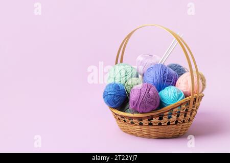 Viele bunte Strickbälle in einem Korb mit Stricknadeln auf einem pastellfarbenen lila Hintergrund. Set für das Hobbys, warme Kleidung oder Spielzeug zu stricken. C Stockfoto