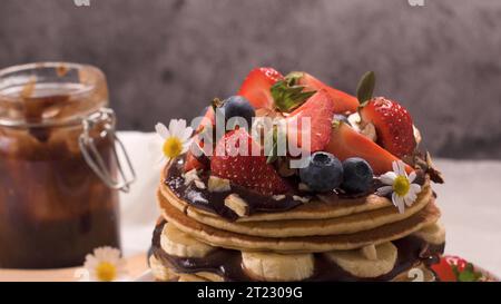 Pfannkuchen mit Banane, Heidelbeeren, Erdbeeren und Schokoladensauce auf einem Teller. Stockfoto