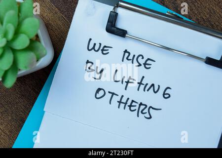 Konzept: Wir erheben uns, indem wir andere heben, schreiben auf Unterlagen, die auf Holztisch isoliert sind. Stockfoto