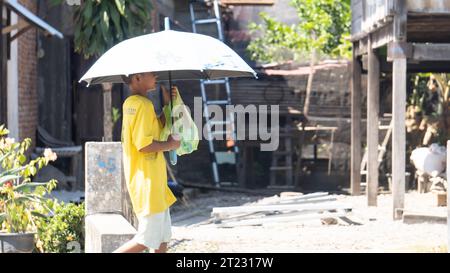 Pinrang Indonesia, 16. Oktober 2023: Ein Junge läuft mit einem Sonnenschirm unter der sengenden heißen Sonne. Nachmittag im Dorf Masolo Pinrang, Indonesien Stockfoto