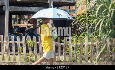 Pinrang Indonesia, 16. Oktober 2023: Ein Junge läuft mit einem Sonnenschirm unter der sengenden heißen Sonne. Nachmittag im Dorf Masolo Pinrang, Indonesien Stockfoto