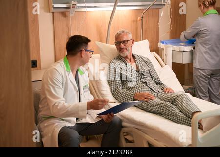 Der Therapeut kommuniziert mit einem alten Mann auf einer Krankenhausstation Stockfoto
