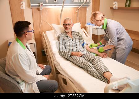 Eine Pflegefachkraft lässt einen grauhaarigen alten Mann infundieren Stockfoto