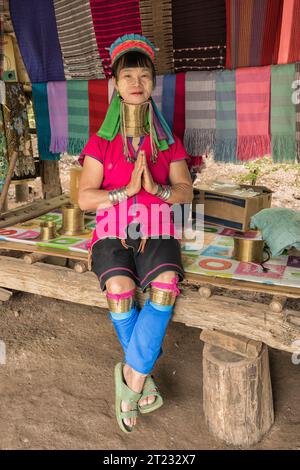 Karen Frau aus Pai in Mae Hong Son, Thailand, mit Messing Halsringen sitzt auf einer Holzschaukel im rustikalen Dorf und trägt ein farbenprächtiges Karen Kleid Stockfoto