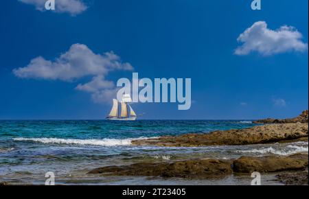 Meereslandschaft mit alter Segelyacht mit weißen Segeln am blauen Himmel mit weißen Wolken. Landschaft der Küste von La Chiappa, Porto-Vecchio, Korsika, Fran Stockfoto