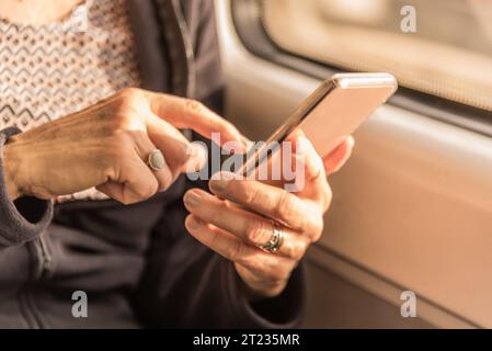 Die Hände der blonden, Reifen Frau nähern sich und schreiben im Zug eine SMS auf dem Handy Stockfoto