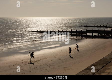 Silhouettenfiguren, die am Strand am Meer Cricket spielen Stockfoto