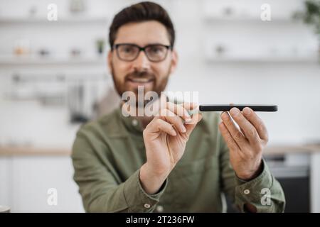 First-Person-Ansicht eines lächelnden männlichen Bloggers in Brillen, der neue moderne Smartphones für Abonnenten in sozialen Medien überprüft. Begriff des Menschen, tec Stockfoto