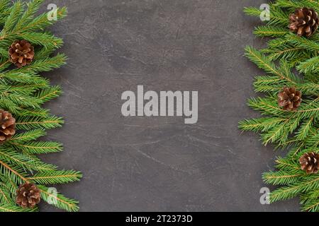 Weihnachtshintergrund mit Weihnachtsbaumzweigen auf einem dunklen strukturierten Hintergrund. Rahmen aus Tannenzweigen, Fichtenzapfen. Neujahrsgrenze auf schwarzem Ba Stockfoto