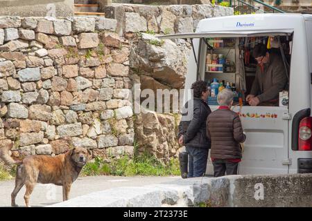 Zwei Frauen in Ocana, Korsika, Frankreich, kaufen in einem Kleinbus ein, der abgelegene Bergdörfer bedient, in denen es keine Geschäfte gibt. Ein Hund beobachtet. Stockfoto