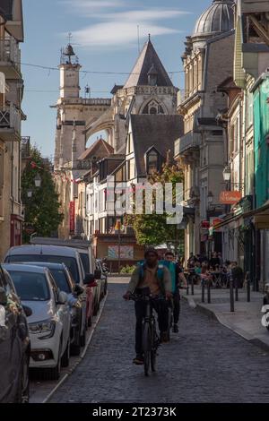 Zwei Männer radeln eine Kopfsteinpflasterstraße in Troyes, Frankreich, mit der Kirche Saint-Jean-au-marché und Fachwerkhäusern im Hintergrund. Stockfoto