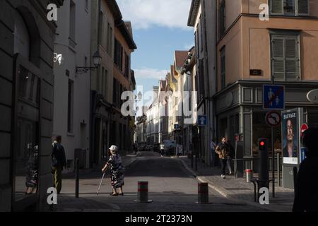 Eine ältere, gehütete Dame mit Krücken überquert die Straße in Troyes, Frankreich, und ihr Bild spiegelt sich in einem Schaufenster wider. Stockfoto