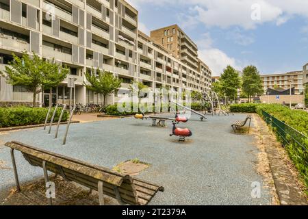 Ein leerer Spielplatz in der Mitte eines großen Apartmentgebäudes mit mehreren Kindern, die auf Schaukeln und Schaukelgeräten spielen Stockfoto