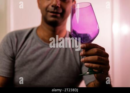 Fremder, nicht erkennbarer, erwachsener kaukasier bittet um ein Getränk mit einem leeren, bunten Weinglas. Stockfoto