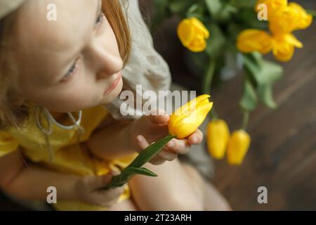 Blick von oben auf ein Mädchen, das eine Tulpe in den Händen hält und zwischen den Tulpen sitzt. Selektives Schärfen. Schärfe an einer Tulpe in den Händen. Stockfoto