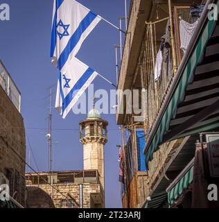 Die israelischen Flaggen sind auf den Straßen der Altstadt Jerusalems mit dem Moscheminarett im Hintergrund, in Israel. Stockfoto