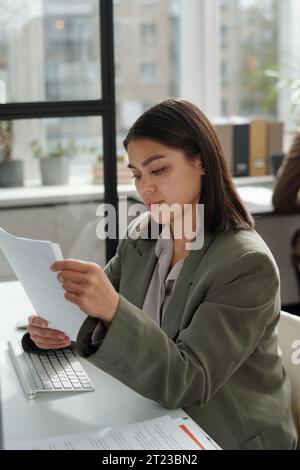 Junge Sekretärin in in formeller Kleidung, die Finanzpapiere durchsucht, während sie Dokumente für Verhandlungen vorbereitet und Geschäftsabschlüsse macht Stockfoto