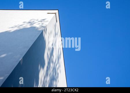 Eine Ecke weißer Wände mit verschwommenem Schattenmuster befindet sich unter blauem Himmel. Abstrakter Architekturhintergrund. Stockfoto