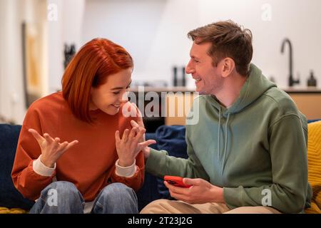 Glückliche überglückte Paarfrau, die gute Nachrichten im Smartphone liest und zu Hause auf der Couch sitzt. Stockfoto