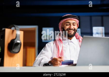 Ein arabischer Geschäftsmann arbeitet fleißig an einem modernen Schreibtisch und schreibt auf seinem Laptop. Er surft im Internet, kommuniziert per E-Mail und leistet Online-Zahlungen mit einer Kredit- oder Debitkarte. Stockfoto