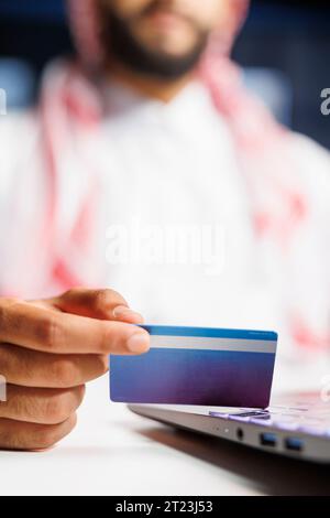 Geschäftsmann in islamischer Kleidung, arbeitet im Büro an seinem Laptop. Er betreibt Online-Forschung, Kommunikation und sichere Online-Einkäufe mit Kredit- und Debitkarten und nutzt dabei die drahtlose Technologie. Stockfoto