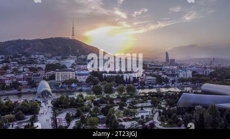 Fantastischer Blick auf die Stadt Tiflis mit dem Fluss Kura, der Fußgängerbrücke des Friedens, dem Rike Park (Leute laufen), dem Wolkenkratzer (Hotel?) Stockfoto