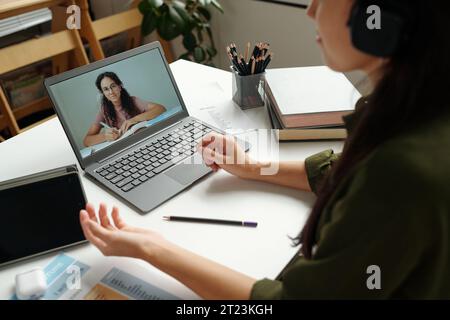 Konzentrieren Sie sich auf den Bildschirm des Laptops, während das clevere Schulmädchen Notizen in einem Copybook macht und während des Online-Unterrichts den Lehrern die Erläuterung des Themas zuhört Stockfoto