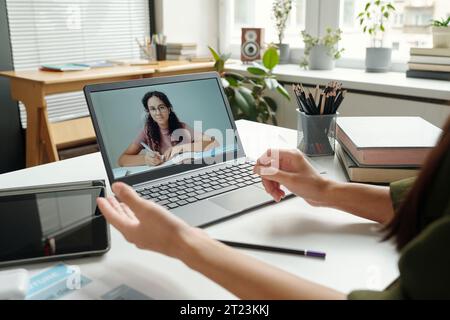 Clevere multiethnische Schülerin auf Laptop-Bildschirm, die den Lehrer ansieht, wie er Grammatikregeln erklärt, und ihr während des Online-Unterrichts zuhört Stockfoto