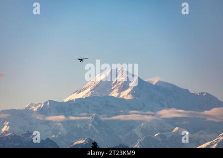 Ein kleines Flugzeug fliegt vor einem großen, schneebedeckten Berg. Stockfoto