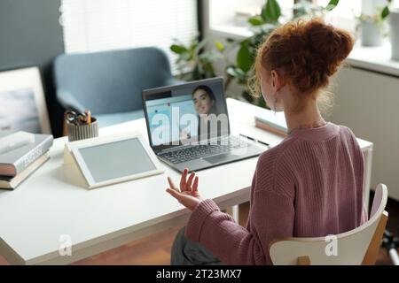 Rückansicht eines cleveren Schulmädchens in Casualwear, das mit dem Lehrer auf dem Laptop-Bildschirm kommuniziert und dabei neue Regeln der englischen Grammatik diskutiert Stockfoto