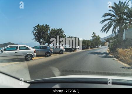 Die Autos hielten am Straßenrand an und fuhren in Agios Nikolaos, Palmen und Seeblick. Hochwertige Fotos Stockfoto
