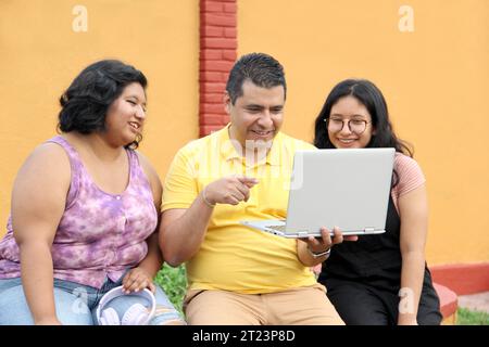 Dunkelhäutige Latino-Papa und -Töchter nutzen ihr Notebook zusammen und verbringen Zeit mit Spielen, Hausaufgaben, Lernen und Videos Stockfoto