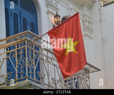 Goldene Stern rote Nationalflagge von Vietnam, die stolz vom Balkon eines Hauses im französischen Kolonialstil in der Altstadt von Hanoi weht Stockfoto