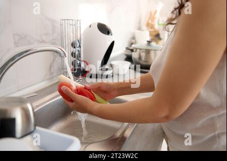 Nahaufnahme der Hände einer Frau, einer Hausfrau, die Gemüse wäscht - frische organische saftige Tomaten und Lauch unter fließendem Wasser im Wasserhahn, die Zubereitung gesunder r Stockfoto