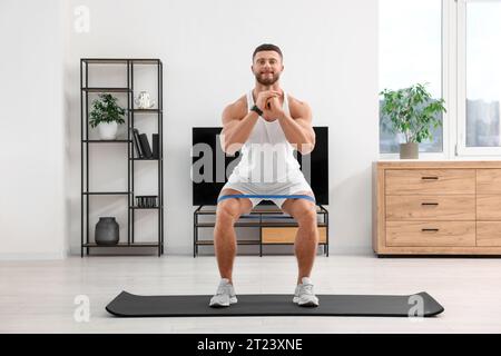 Sportlicher Mann, der zu Hause mit elastischem Widerstandsband auf der Matte Sport macht Stockfoto