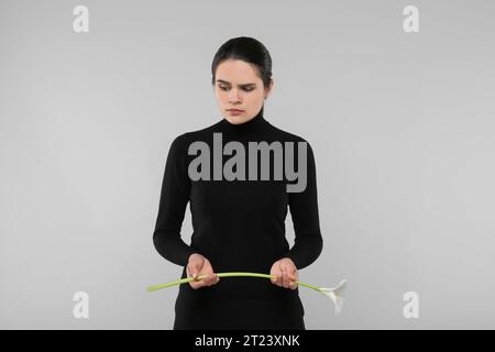 Traurige Frau mit Calla-Lilienblume auf hellgrauem Hintergrund. Trauerfeier Stockfoto