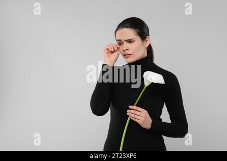 Traurige Frau mit Calla-Lilienblume, die auf hellgrauem Hintergrund trauert, Platz für Text. Trauerfeier Stockfoto