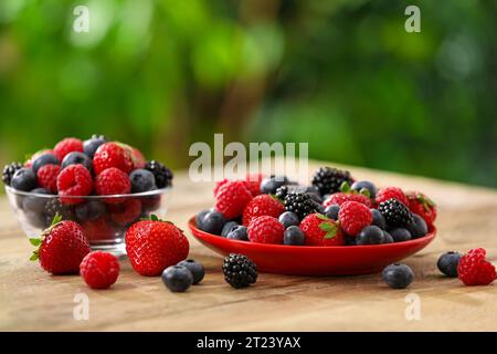Verschiedene frisch reife Beeren auf Holztisch draußen Stockfoto