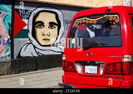 Ein roter Minibus mit Rosetten in den Farben der bolivianischen Nationalflagge fährt an einem Wandbild vorbei, das die Unterstützung für ein freies Palästina, Miraflores Viertel, La Paz, Bolivien zeigt. Das Foto wurde im September 2018 aufgenommen. Stockfoto