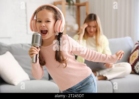 Lautes kleines Mädchen in Kopfhörern mit Mikrofon, das zu Hause singt Stockfoto