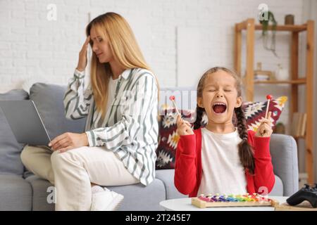 Lautes kleines Mädchen, das Xylophon spielt, und ihre arbeitende Mutter zu Hause Stockfoto