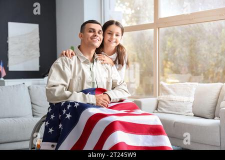 Kleines Mädchen mit ihrem Vater im Rollstuhl zu Hause. Feierlichkeiten zum Veteranentag Stockfoto