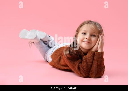 Niedliches kleines Mädchen in warmem Pullover, das auf rosa Hintergrund liegt Stockfoto